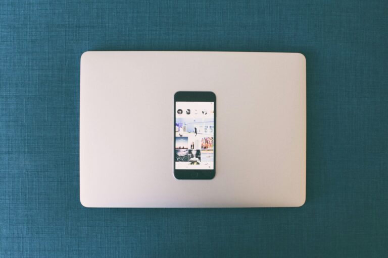Flat lay of a smartphone on a laptop with social media photos on screen.